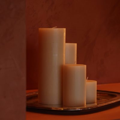 Cuatro velas blancas de diferentes alturas sobre una bandeja metálica en un espacio cálido, ambientando la experiencia Regala masaje Madrid.